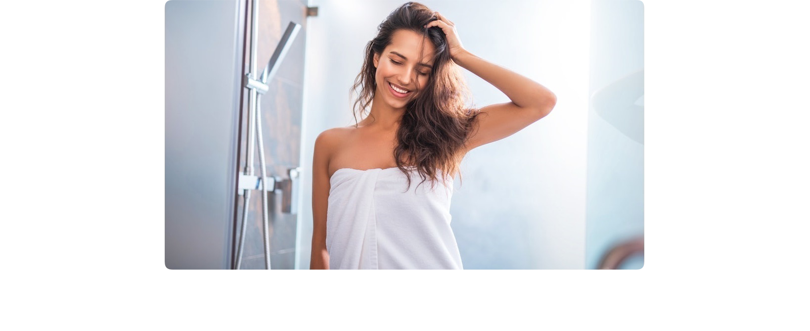 Smiling woman coming out of the shower wrapped in white towel